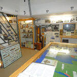 Exhibition room with display cases, weapons, and historical photographs from the Second World War