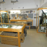 Exhibition room with display cases, weapons, and historical photographs from the Second World War