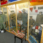 Ausstellung zur Bundeswehr mit Soldatenuniformen, Ausrüstung und militärischem Arbeitsbereich in einer Museumsvitrine